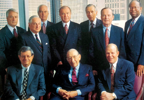 Grainy photograph of men sitting and standing, smiling at camera