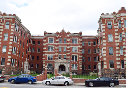 Four-story red apartment building front entrance with cars parked in front