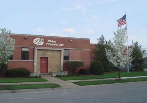 Global Titanium Inc building with white flowered trees and an American flag on a flagpole