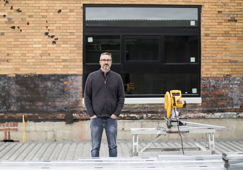 Man standing in front of a brick storefront with a circular saw