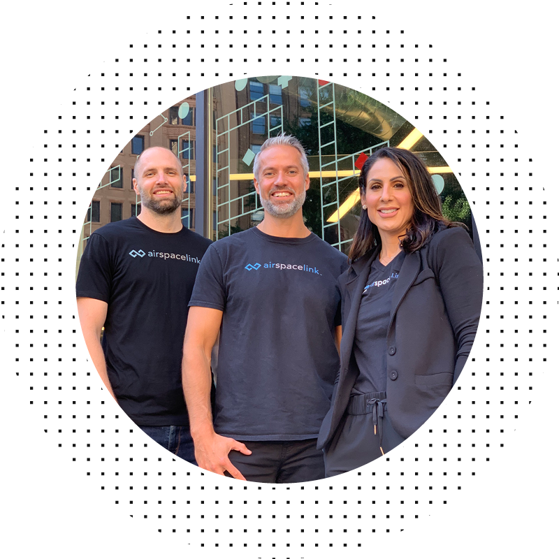 Three people smiling at camera in front of building