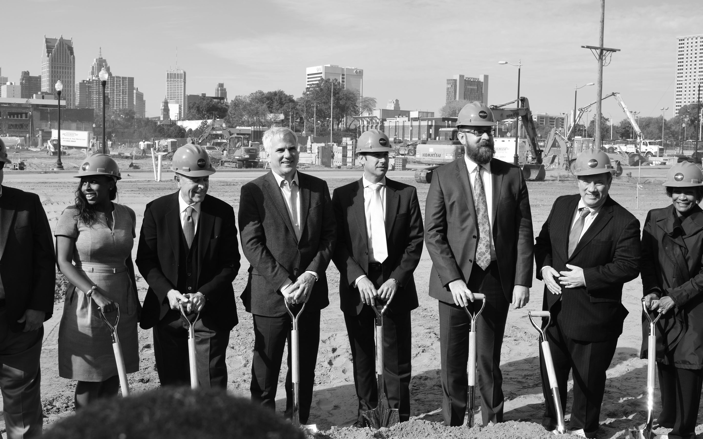 People standing in an empty dirt lot with shovels and hard hats